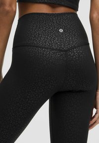 Hoch taillierte, schwarze Leggings aus stretchigem Material mit einem dezenten Leopardenmuster und einem kleinen Logo auf der Rückseite.