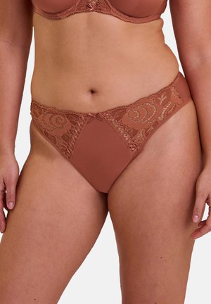 Femme portant un sous-vêtement style bikini en dentelle terracotta et tissu uni avec des motifs floraux et un soutien-gorge assorti.