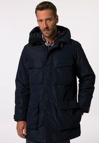 Marinblå, vattentät parka-jacka med flera framfickor, huva och dragkedjestängning. Har en slät yta och ett slitstarkt material.