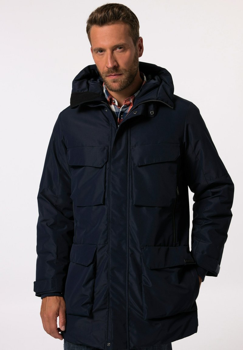 Marinblå, vattentät parka-jacka med flera framfickor, huva och dragkedjestängning. Har en slät yta och ett slitstarkt material.