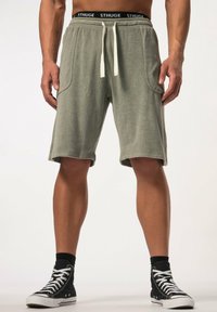 Pantalones cortos de toalla verde con cinturilla elástica, cordón blanco y bolsillos laterales, combinados con zapatillas altas negras.