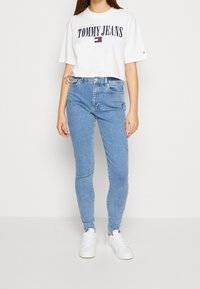 Camiseta corta blanca con el logo "TOMMY JEANS", combinada con jeans skinny azul claro y zapatillas blancas. Tejido suave, ajuste casual y estilo b�ásico.