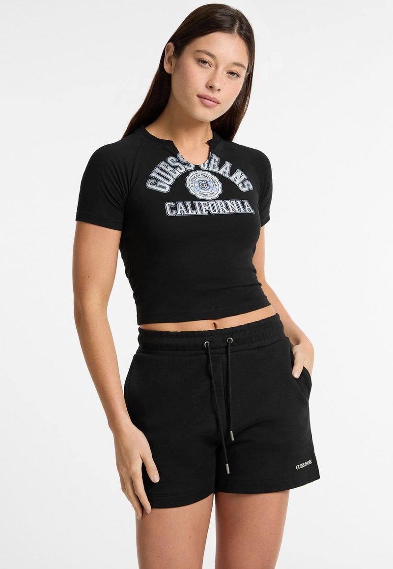 Čierne skrátené tričko s okrúhlym výstrihom a krátkymi rukávmi, na ktorom je biely a modrý grafický motív "Guess Jeans California". Skombinované s čiernymi šortkami na šnúrku.
