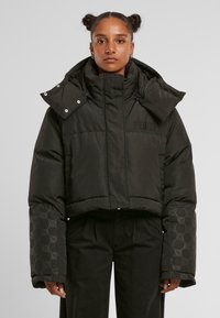 Sort cropped puffer-jakke med høj krave, der har et tekstureret mønster på ærmerne og logo-broderi. Glat, polstret stof.