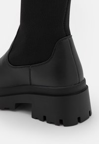 Mustat nilkkurit, joissa on teksturoitu päällinen, sileät nahkaosat ja paksu, kestävä pohja, jossa on voimakkaat urat.