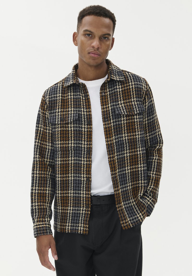 Karirana srajca z modro, rjavo in smetanasto barvno shemo, izdelana iz teksturirane tkanine, z dvema sprednjima žepoma in ovratnikom.