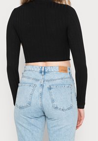 Black ribbed crop top with long sleeves paired with light blue high-waisted jeans featuring a brown label on the waistband.