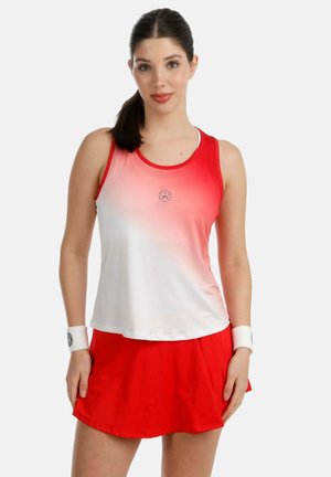 Frau trägt rotes und weißes ärmelloses Sportoberteil, roten Rock und weiße Handgelenkbänder, steht vor einfachem hellem Hintergrund.