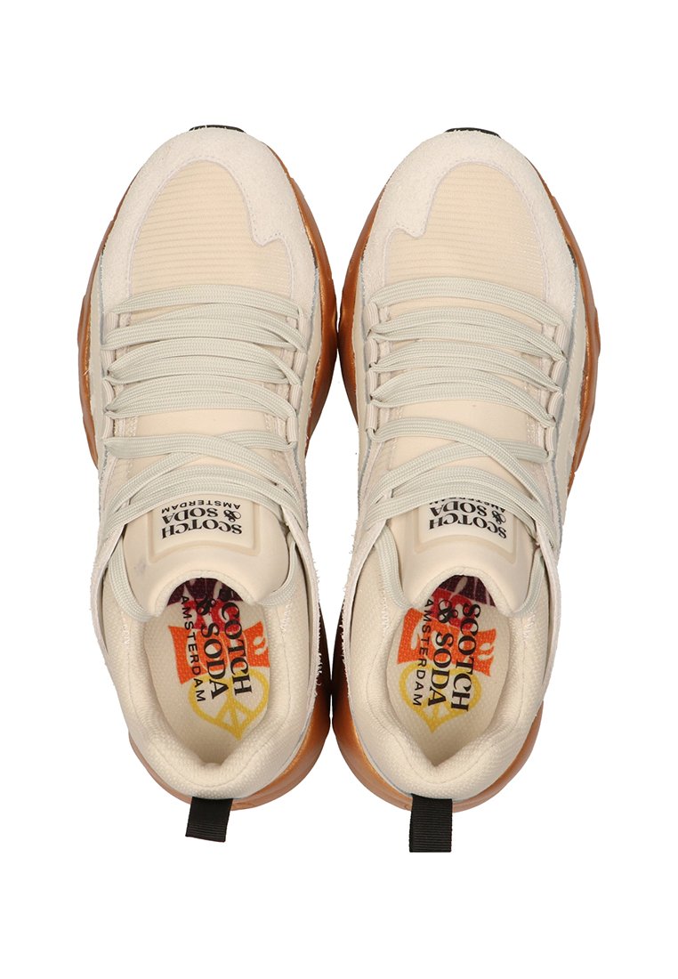 Baskets de sport beiges avec une tige texturée, des lacets élastiques et une semelle en caoutchouc brun. Présente un logo sur la languette et des semelles intérieures colorées.