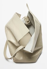 Beige leather tote bag with a soft texture, open top, and a contrasting gray lining. Features a single strap and minimalistic design.