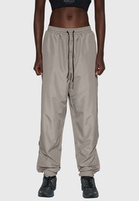 Lätta, beige, vattentäta joggerbyxor med elastiska muddar och linning; dragsko i midjan; används med svarta, robusta skor.