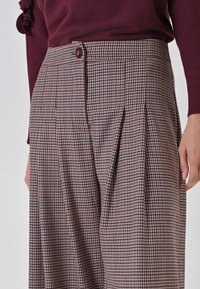 Braun- und graue Karohosen mit Falten und einer kastanienbraunen Knopf. Strukturiertes Gewebe, hoch geschnittenes Design und taillierte Passform.