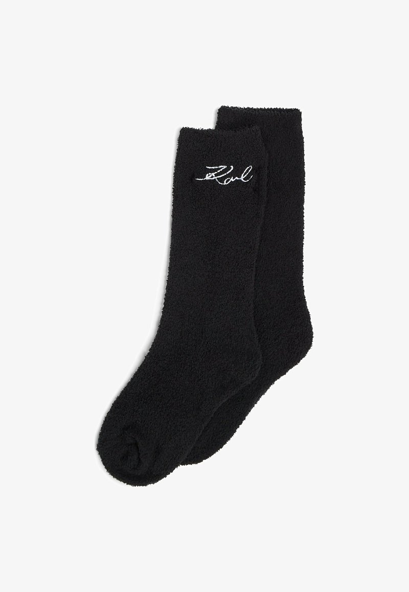 Paire de chaussettes noires duveteuses avec un texte en cursive blanc brodé près du haut sur un fond blanc uni.