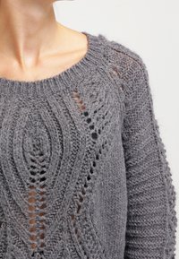 Gray knitted sweater featuring a loose design, textured patterns, and open stitches, with a wide neckline and long sleeves.