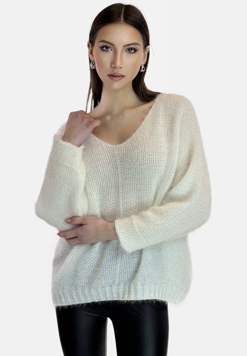 Witte, oversized gebreide trui met een diepe V-hals, lange mouwen en een losse pasvorm. Textuur van het garen en geribbelde onderrand zijn zichtbaar.