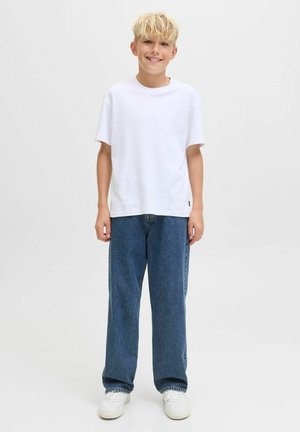 T-shirt blanc à manches courtes associé à un jean en denim bleu ample et des baskets blanches, posé sur un fond clair et uni.