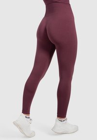 Burgunderfarbene High-Waist-Leggings aus elastischem Material mit glatter Struktur und körpernahem Schnitt, kombiniert mit weißen Sportschuhen.