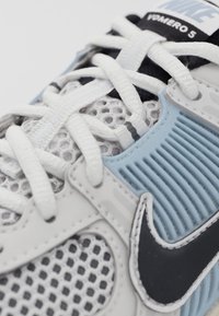 Primer plano de una zapatilla de correr Nike blanca y azul con tela de malla, cordones blancos y logo Swoosh negro en el lateral.