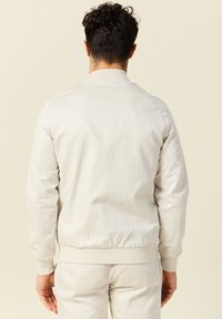 Licht beige bomberjack gemaakt van zachte stof, met ribboorden aan de mouwen en tailleband, voorzien van een schoon, minimalistisch ontwerp.