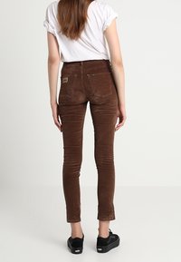 Bruna kordbyxbyxor i slim fit med hög midja, bakfickor och logotyp på höger sida. Matchas med svarta sneakers.