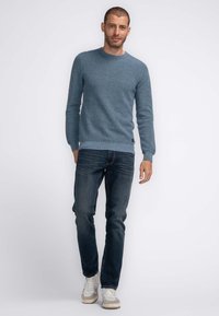 Lichtblauw gebreid sweater met een geribbelde textuur, ronde halslijn en lange mouwen, gecombineerd met donkerblauwe jeans en witte sneakers.