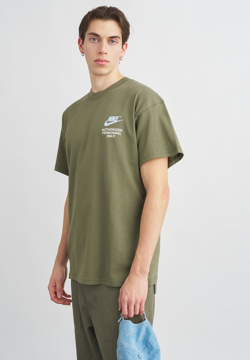 Ελαιοπράσινο βαμβακερό μπλουζάκι με στρογγυλή λαιμόκοψη, κοντά μανίκια και εκτυπωμένο λογότυπο Nike με την ένδειξη "ΜΟΝΟ ΕΞΟΥΣΙΩΜΕΝΟΙ ΑΤΟΜΟΙ".