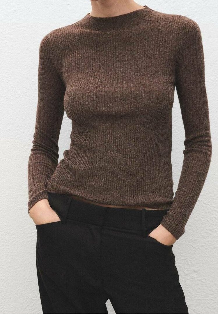 Personne portant un haut marron ajusté à manches longues côtelé, rentré dans un pantalon noir taille haute, les mains dans les poches.