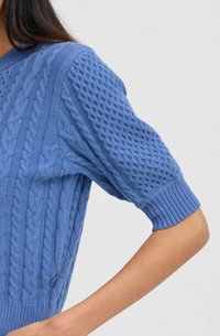 Hellblaut gestrickter Pullover mit kurzen Ärmeln, der ein strukturiertes Muster und gerippte Bündchen aufweist, aus weichem, leichtem Material gefertigt.