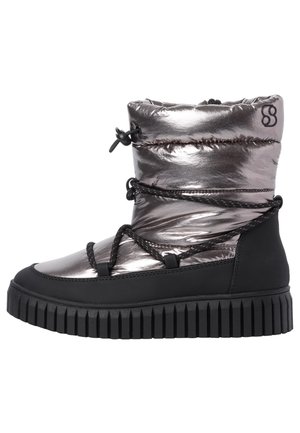 Metaliczne srebrne zimowe buty z czarną grubą podeszwą, czarnymi sznurowadłami wokół kostki i ściągaczem przy mankiecie.