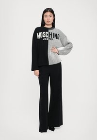 Juodas ir pilkas dryžuotas megztinis su įragiu tekstūra, puošiamas "Moschino Jeans" logotipu. Derinamas su plačiomis juodomis kelnėmis.