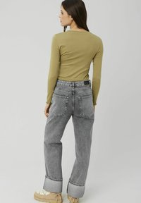 Haut à manches longues olive avec un pantalon en jean gris clair taille haute, présentant des poignets retroussés et deux poches arrière.