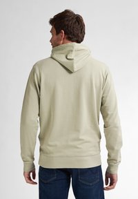 Sudadera verde claro con bolsillo tipo canguro, capucha ajustable, puños y dobladillo acanalados, combinada con jeans azul oscuro, vista desde la parte posterior.