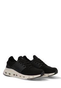 Zapatillas deportivas negras con parte superior de malla, acentos texturizados, cordones planos y una suela blanca con amortiguación que presenta cortes circulares para ventilación.