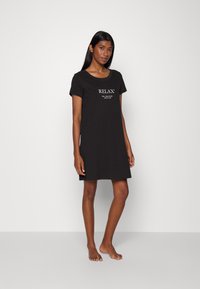 Čierna nočná košeľa s krátkym rukávom, okrúhlym výstrihom a stredovým nápisom "RELAX" spolu so sloganom. Vyrobená z mäkkého, priedušného materiálu.
