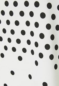 Tissu blanc avec des pois noirs uniformément espacés formant un motif régulier.