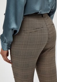 Bruna rutig skräddarsydda byxor med en bakficka, kombinerat med en blå satinskjorta med långa ärmar och knäppta manschetter.