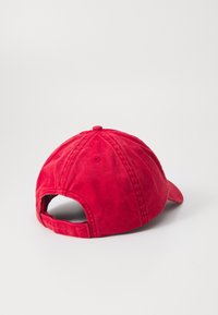 Red cotton baseball cap with a curved brim, adjustable strap at the back, and six ventilation eyelets for breathability.