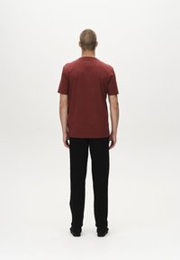 Herre kortærmet vinrød skjorte med rund halsudskæring, kombineret med sorte bukser og sorte sko, set bagfra.