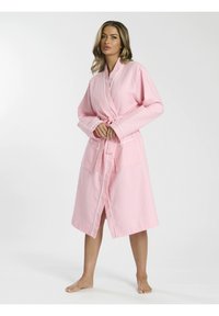 Robe texturée en waffle rose clair avec une taille à nouer, des manches longues et des piping blancs. Elle possède deux poches avant et est coupée au niveau du genou.