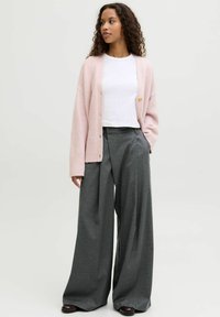 Rozā adīta kardigāna ar brīvu piegriezumu un pogām, kopā ar pelēkām, platām, rakstainām biksēm. Zemāk valkāta balta T-krekla ar apaļu kakla izgriezumu.