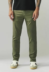 Roheline puuvillane püksid slim fit lõikega, millel on sile tekstuur. Koos valgete tossudega ja musta T-särgiga.