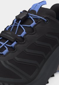 Juoda sportinė avalynė su mėlynomis elastingomis raištelėmis be rišimo, raištelių laikikliu ir tvirtu tekstūruotu padu, skirtu lauko naudojimui.