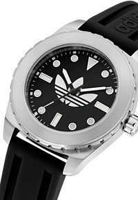 Montre analogique noire avec un boîtier en acier inoxydable, un cadran noir, des index d'heure argentés et un bracelet en caoutchouc noir. Présente le logo Adidas.