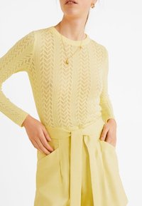 Maglione lavorato a maglia di colore giallo chiaro con motivo a zig zag e maniche lunghe, abbinato a pantaloni a vita alta dello stesso colore e cintura con fiocco.