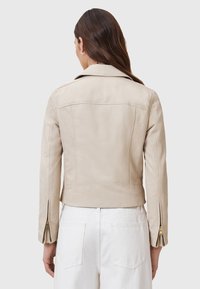 Giubbotto in pelle beige con design aderente, caratterizzato da un inserto posteriore, polsini con zip e dettagli di cucitura minimi per un aspetto elegante.