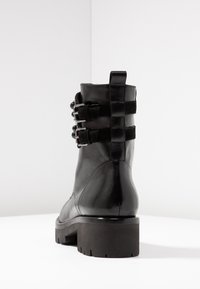 Stivale alla caviglia in pelle nera con suola spessa, caratterizzato da tre cinturini decorativi e fibbie metalliche lungo il lato. Finitura liscia e strutturata.