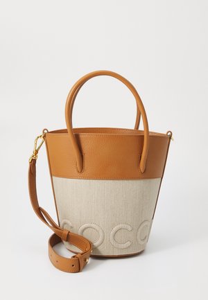 Bruine leren en beige canvas emmer tas met dubbele handvatten, verstelbare schouderband en ingedrukte "COCO" details aan de voorkant.