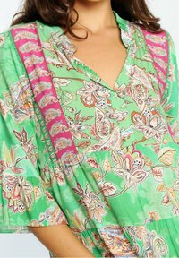 Vestido floral verde con escote en V, mangas amplias y un panel rosa en contraste, adornado con intrincados patrones de paisley y flores.