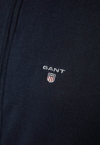 Close-up of navy blue knitted fabric with white GANT logo and a small shield emblem with stars and stripes.