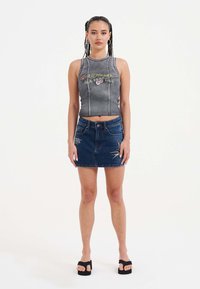 Šedý žebrovaný crop top s květinovou výšivkou, spárovaný s modrou denimovou mini sukni s švy a kapsami. Černé platformové sandály.